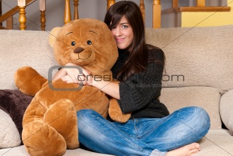 Young woman embracing teddy bear sitting on sofa