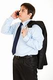 Thoughtful young businessman with jacket on his shoulder talking on mobile phone

