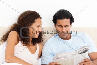 Happy woman looking at her serious boyfriend reading the newspaper
