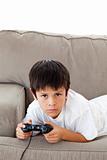 Concentrated boy playing video games lying on the sofa