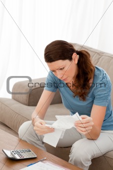 Worried woman looking at her bills sitting on her sofa