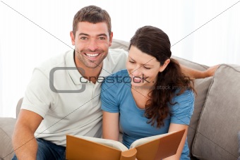 Pretty woman reading a book with her boyfriend on the sofa