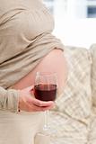 Close up of a pregnant woman at home with a glass of red wine