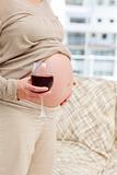 Close up of a pregnant woman at home with a glass of red wine