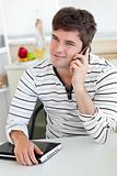 Delighted man talking on phone using his laptop in the kitchen