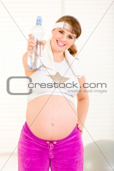 Smiling beautiful pregnant woman in sportswear holding bottle of pure water
