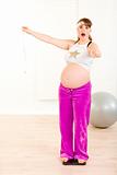 Shocked pregnant woman standing on weight scale and holding  measure tape
