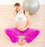 Smiling beautiful pregnant woman in sportswear sitting on floor and holding her belly
