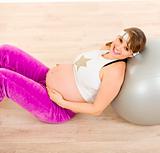 Smiling beautiful pregnant woman sitting on floor and relaxing after exercising 
