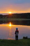 The boy on the shore of lake at sunset