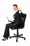 Smiling modern business woman sitting on  chair with  laptop and showing victory gesture
