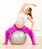 Smiling beautiful pregnant woman doing exercises on  fitness ball at home
