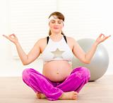 Beautiful pregnant woman doing yoga on floor at home
