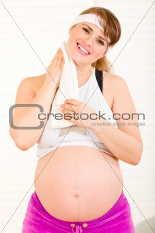 Beautiful pregnant woman wiping her face with towel after exercising at home
