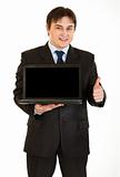  Smiling young businessman holding laptop with blank screen and showing  thumbs up gesture
