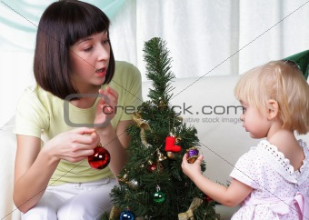 Mum and her small daughter decorate a christmas fur-tree