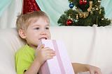 Little boy near to christmas fur-tree sits with gift