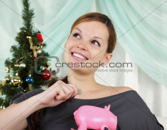 The young beautiful woman sits near a christmas fur-tree and thinks about her savings
