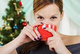 The young beautiful woman sits near a christmas fur-tree with a red cup 
