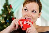 Woman sits near a christmas fur-tree with a red cup