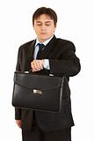 Serious modern businessman with briefcase in hand looking at his watch

