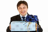 Laughing young businessman holding gift in hands 
