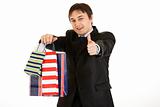 Smiling young businessman holding shopping bags and showing  thumb up gesture
