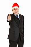 Happy young businessman in Christmas hat showing  thumb up gesture
