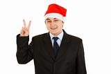 Happy young businessman in Santa hat showing victory gesture.
