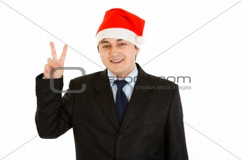 Happy young businessman in Santa hat showing victory gesture.
