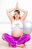 Beautiful pregnant woman doing yoga exercises on floor at home
