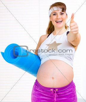 Smiling beautiful pregnant woman with exercise mat showing  thumb up gesture
