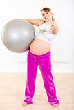 Smiling beautiful pregnant woman holding fitness ball and showing thumbs up gesture
