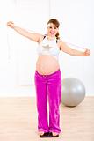 Smiling pregnant woman standing on weight scale and holding  measure tape
