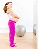 Pregnant woman looking in mirror and measuring  her belly 
