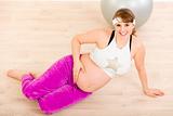 Smiling beautiful pregnant female sitting on floor and relaxing after exercising 
