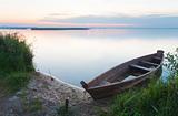 Sunset with old flooding boat on summer lake shore