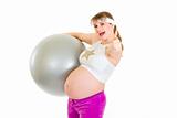 Smiling beautiful pregnant woman holding fitness ball and showing thumbs up gesture
