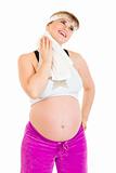Smiling pregnant woman wiping her face with towel after exercising
