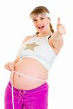 Smiling pregnant woman holding measure tape and showing thumbs up gesture
