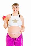 Smiling beautiful pregnant woman measuring her belly and holding apple
