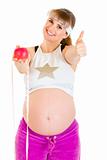 Smiling beautiful pregnant woman with measure tape and apple showing thumbs up gesture
