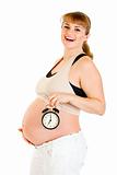 Happy pregnant woman holding alarm clock in front of her belly
