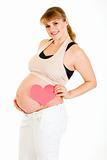 Smiling pregnant woman holding heart near her belly
