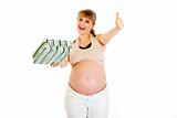 Happy pregnant woman holding gift for her baby and showing thumbs up gesture

