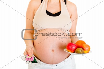 Pregnant woman holding pills and fruits. Close-up.
