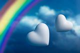 Two hearts and rainbow against a blue sky