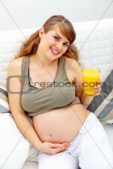 Smiling beautiful pregnant woman sitting on couch with glass of juice  in hand
