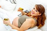 Smiling beautiful pregnant woman relaxing on sofa and eating pickles

