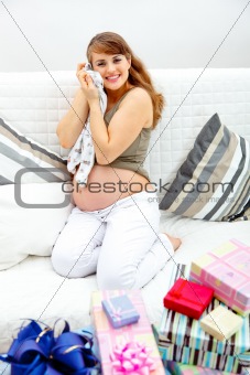 Happy  beautiful pregnant woman sitting on sofa with presents for her unborn baby
